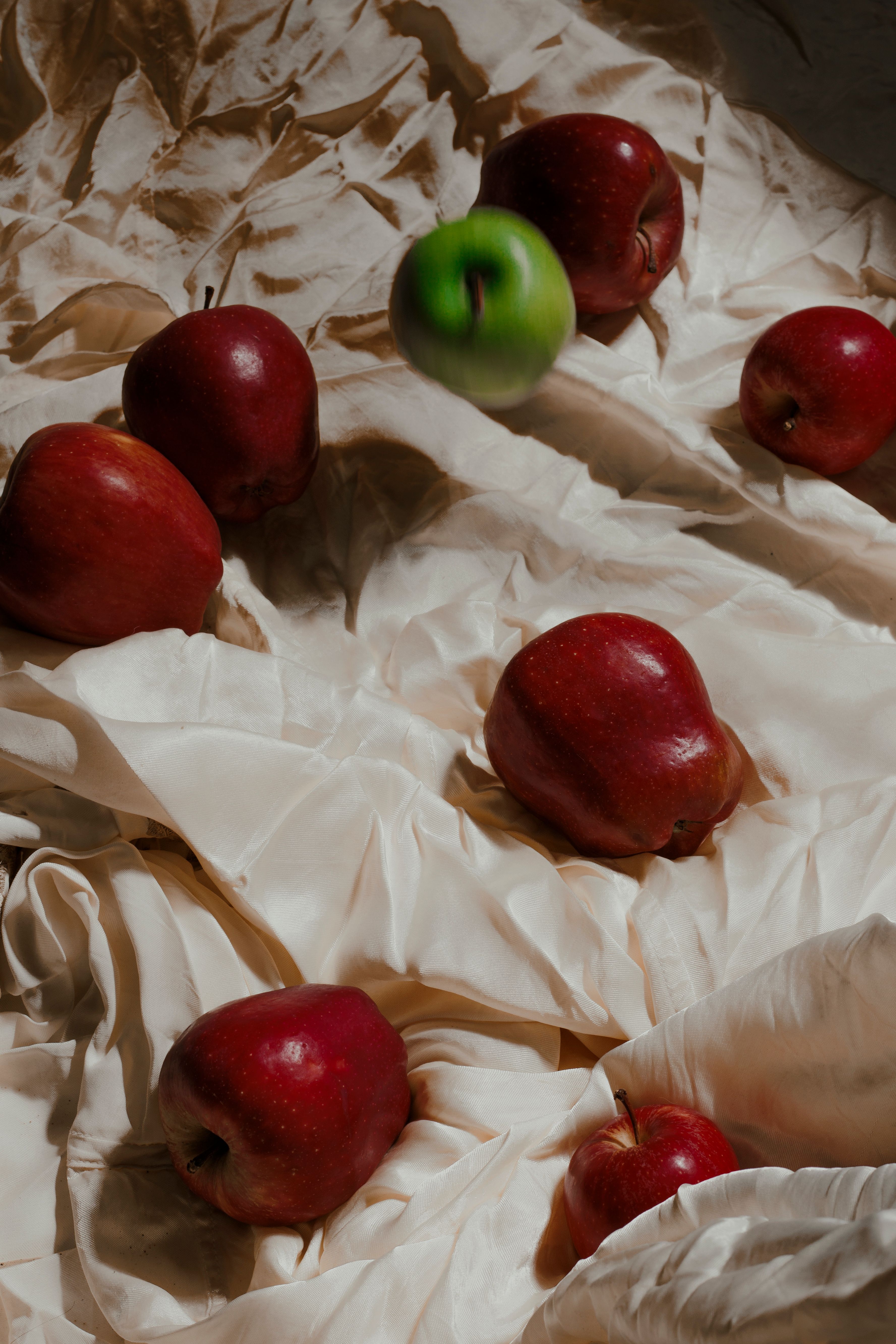 Red and green apples arranged on luxurious cream satin, showcasing natural beauty.