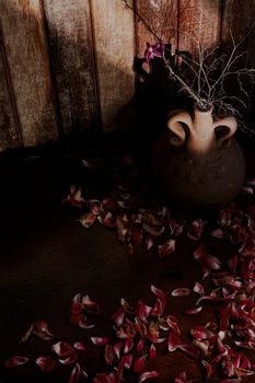 Artistic composition of a rustic vase with scattered petals on a wooden floor.
