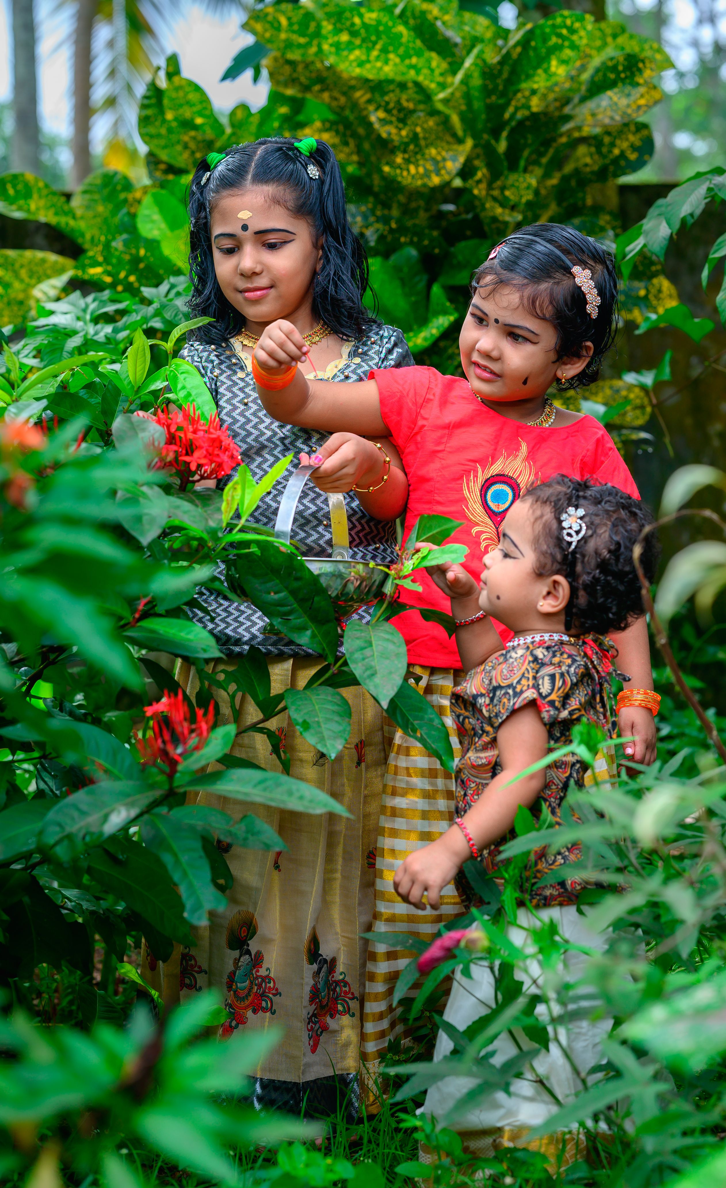 Three young girls exploring vibrant plants in an outdoor garden in India.