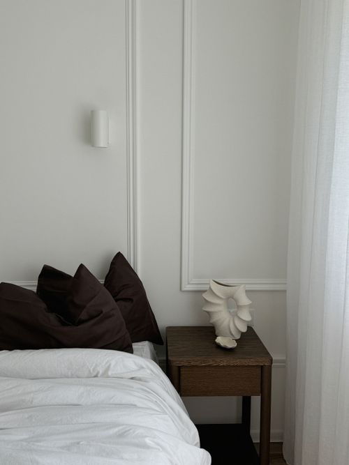 Free A minimalist bedroom corner with dark pillows, nightstand, and ceramic sculpture. Stock Photo