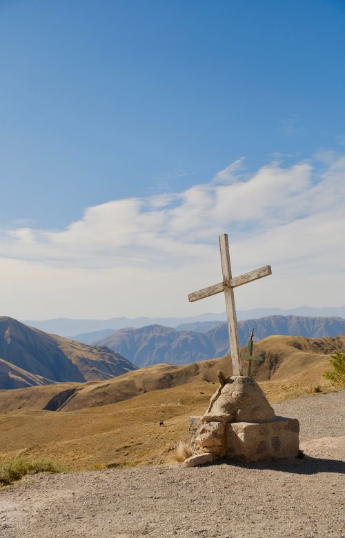 Free A solitary wooden cross along a picturesque mountain trail under a clear blue sky. Stock Photo