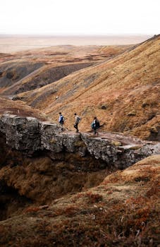 Three hikers with backpacks traverse a rocky pathway through a stunning mountain landscape.