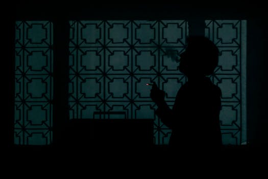 Dark silhouette of a man smoking by a patterned window, creating a moody atmosphere.