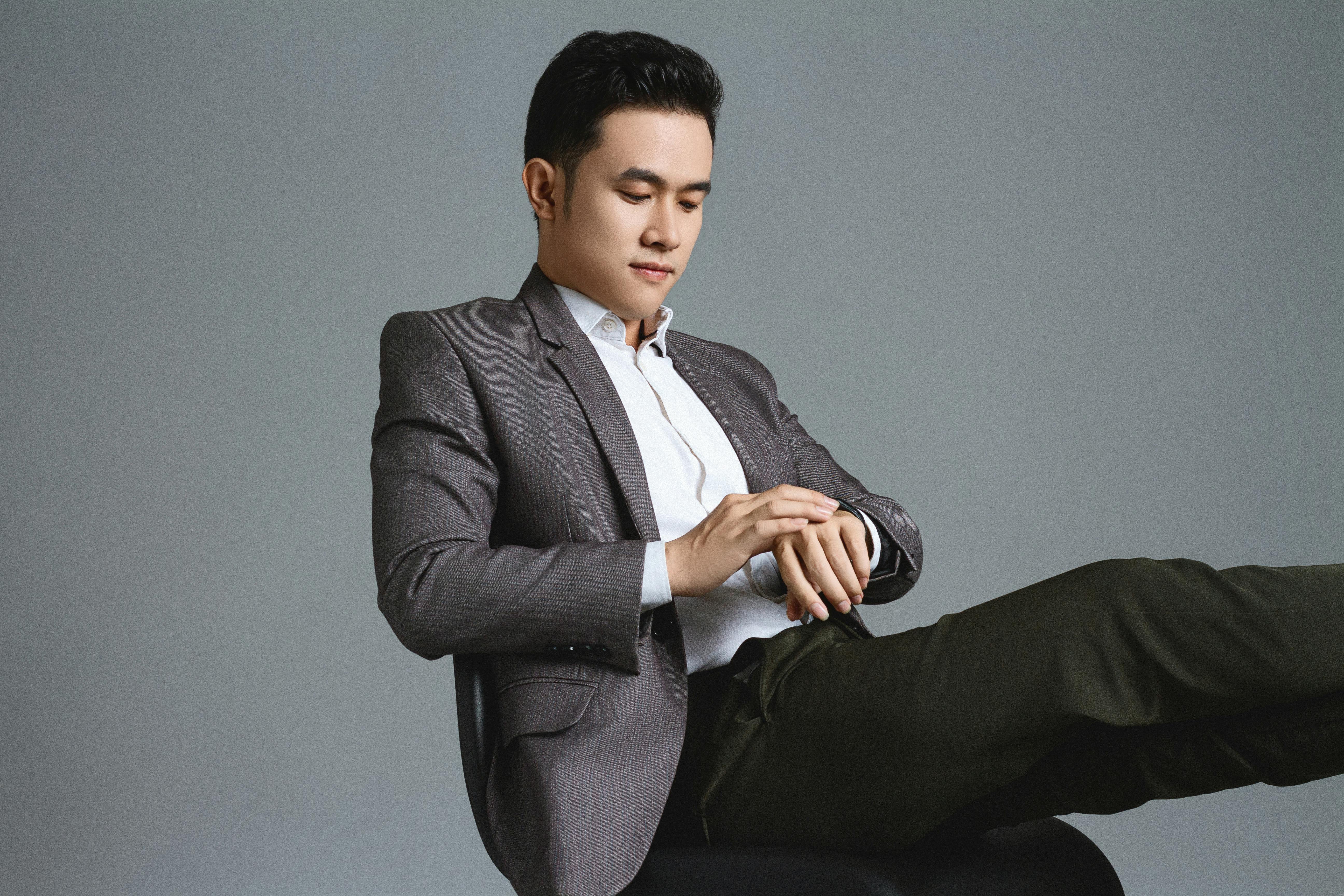 Asian businessman in a stylish suit looking at his watch, sitting in a studio setting.