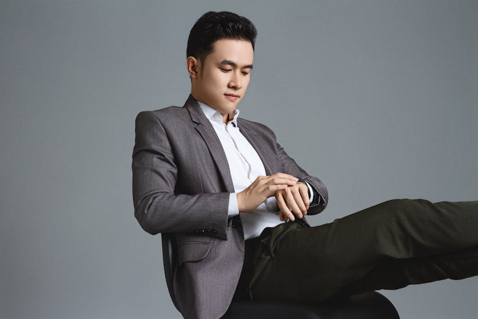 Samsung Galaxy Watch 7 vs Google Pixel Watch 3: Android Fitness Face-off (2024) Asian businessman in a stylish suit looking at his watch, sitting in a studio setting.