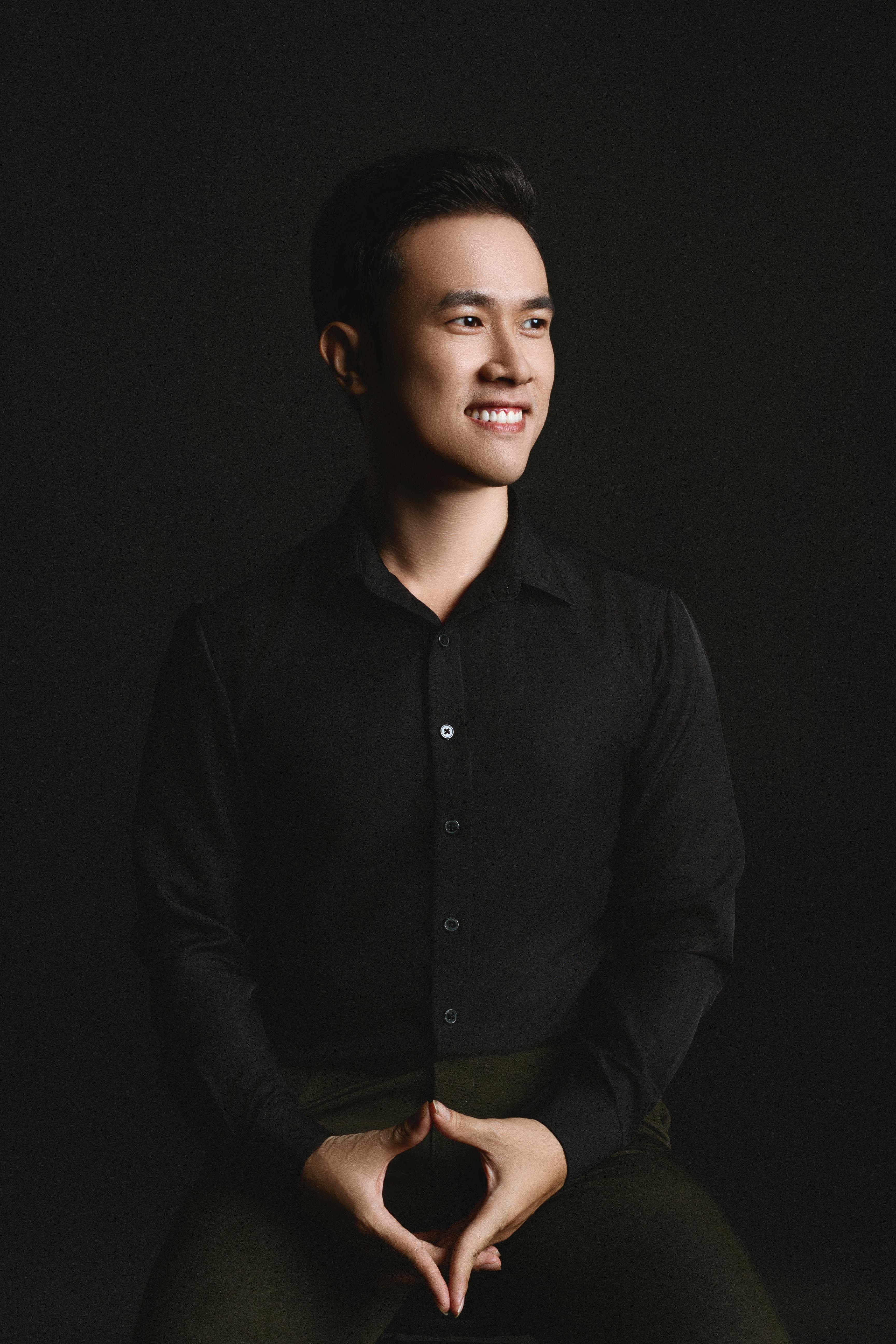 A sophisticated studio portrait of a smiling man in a black shirt, exuding confidence and style.
