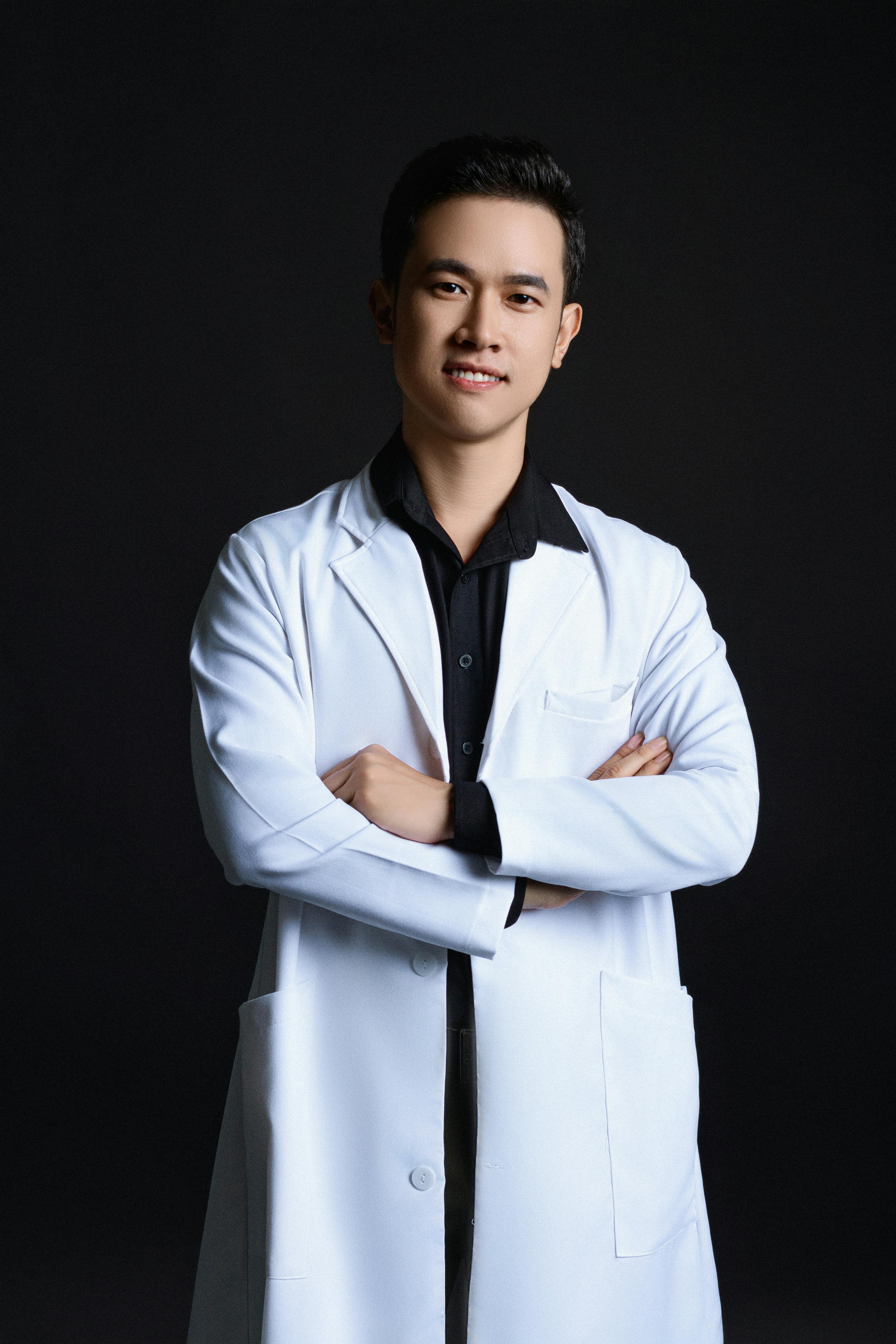 Portrait of a young adult in a lab coat, arms crossed, exuding professionalism.
