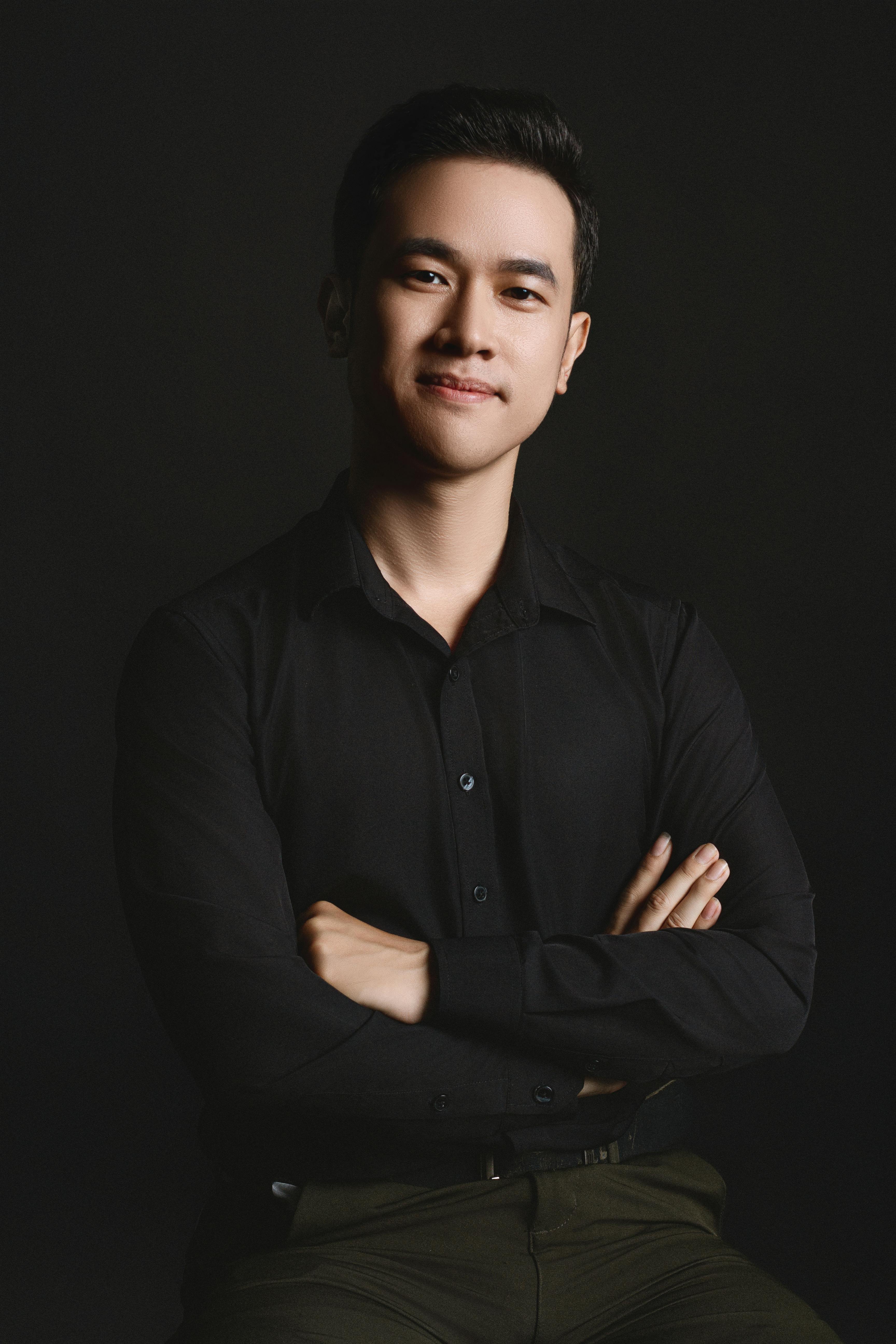 Portrait of a confident young man in a studio setting with a black background and arms crossed, conveying professionalism.