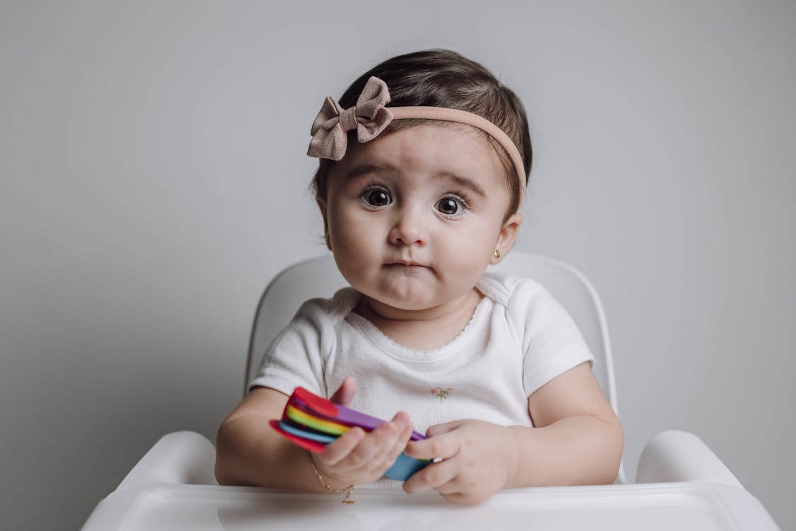 A baby girl sitting in a high chair with a colorful toy