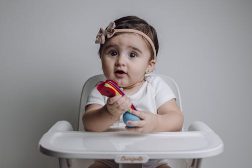 A baby girl sitting in a high chair with a toy