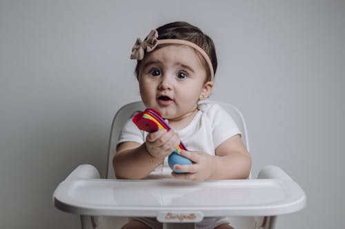 Free A baby girl sitting in a high chair with a toy Stock Photo