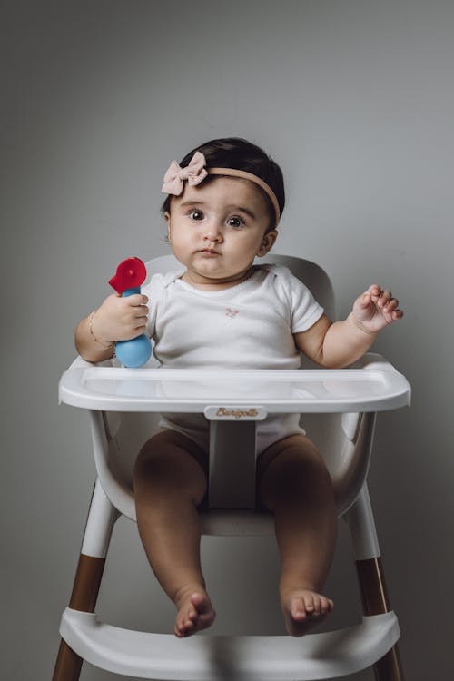 Free A baby girl sitting in a high chair with a flower Stock Photo