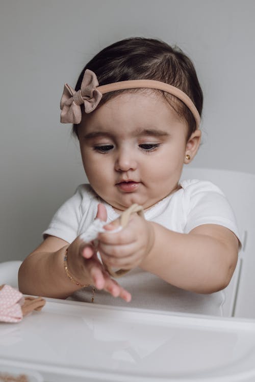 A baby girl is sitting in a high chair with a pink bow