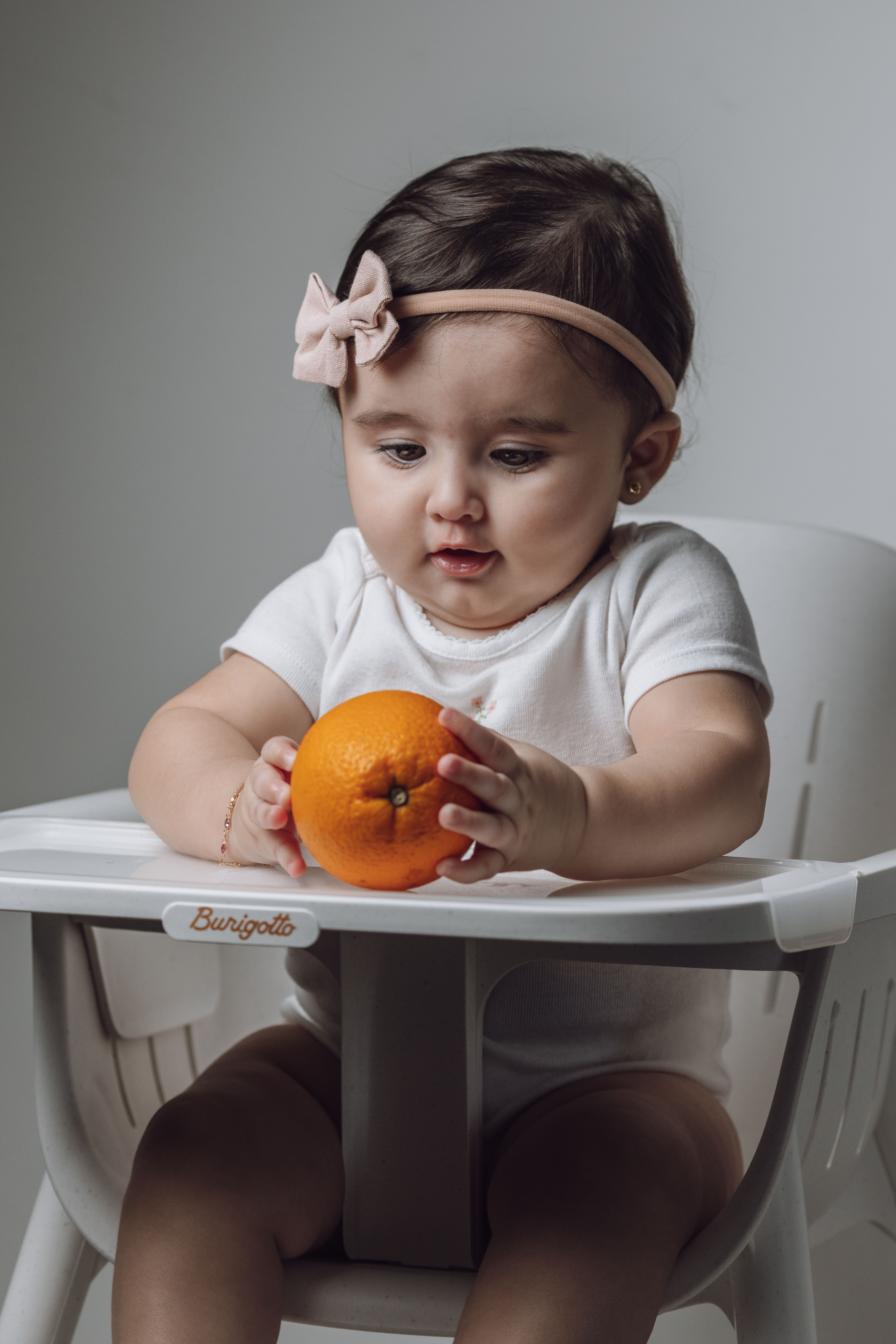 Cute baby playing with an orange in a high chair, studio shot.