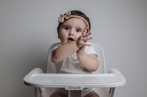 A baby girl sitting in a high chair with her hands up