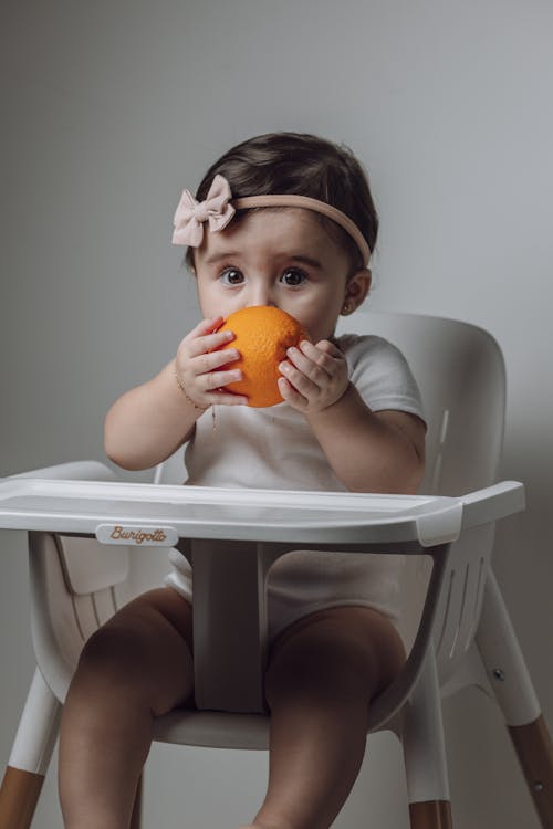 A baby girl sitting in a high chair with an orange