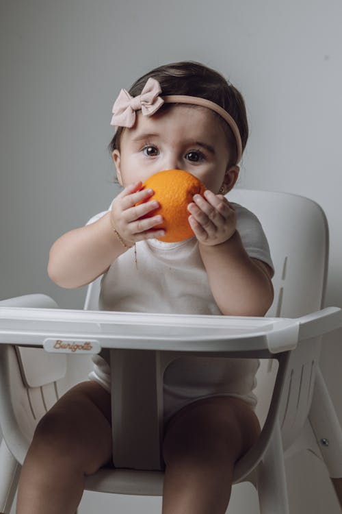 A baby girl is sitting in a high chair with an orange