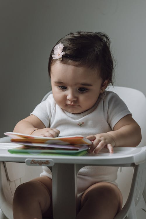 A baby sitting in a high chair reading a book