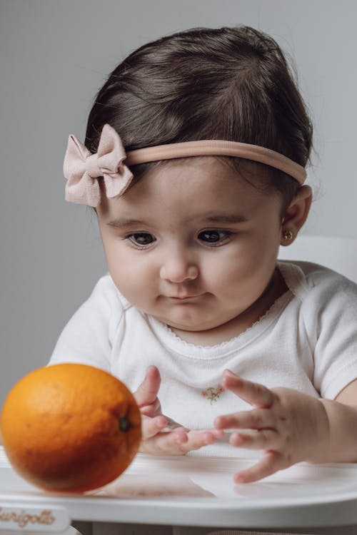 A baby girl is holding an orange in her hand