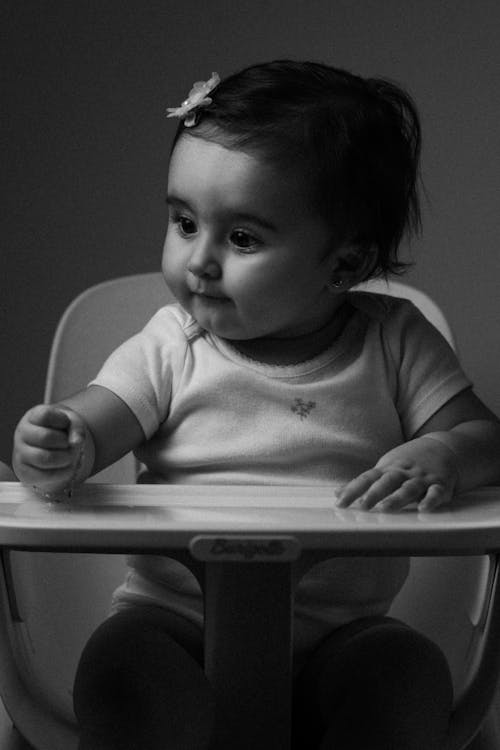 A black and white photo of a baby sitting in a high chair