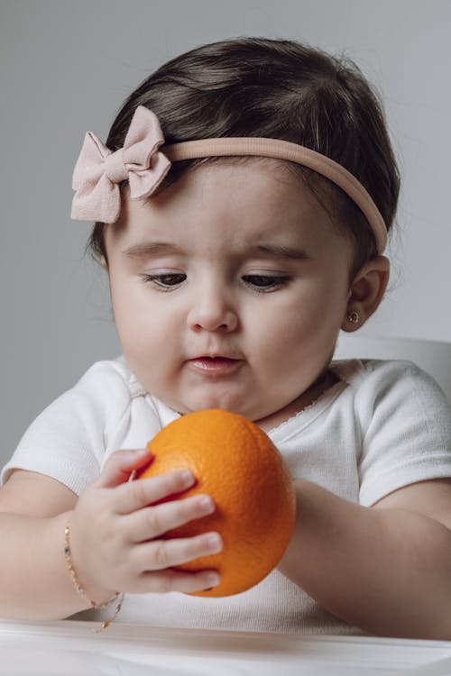 A baby girl holding an orange in her hand
