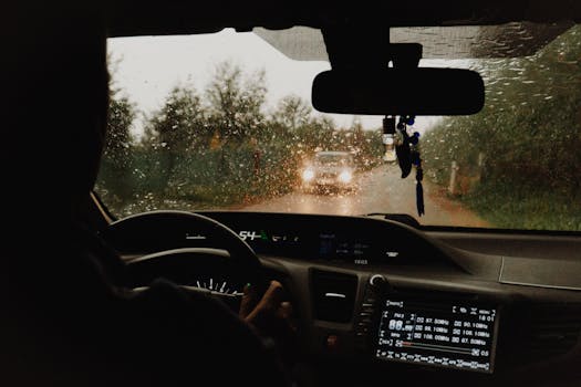 Interior view of a car driving through a rural road in the rain.