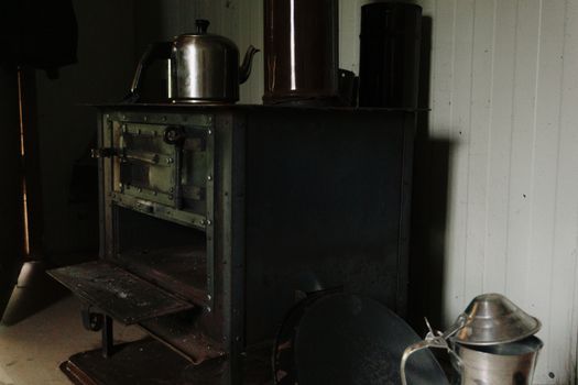 A dimly lit corner featuring a vintage iron stove with a metal kettle on top in a rustic setting.