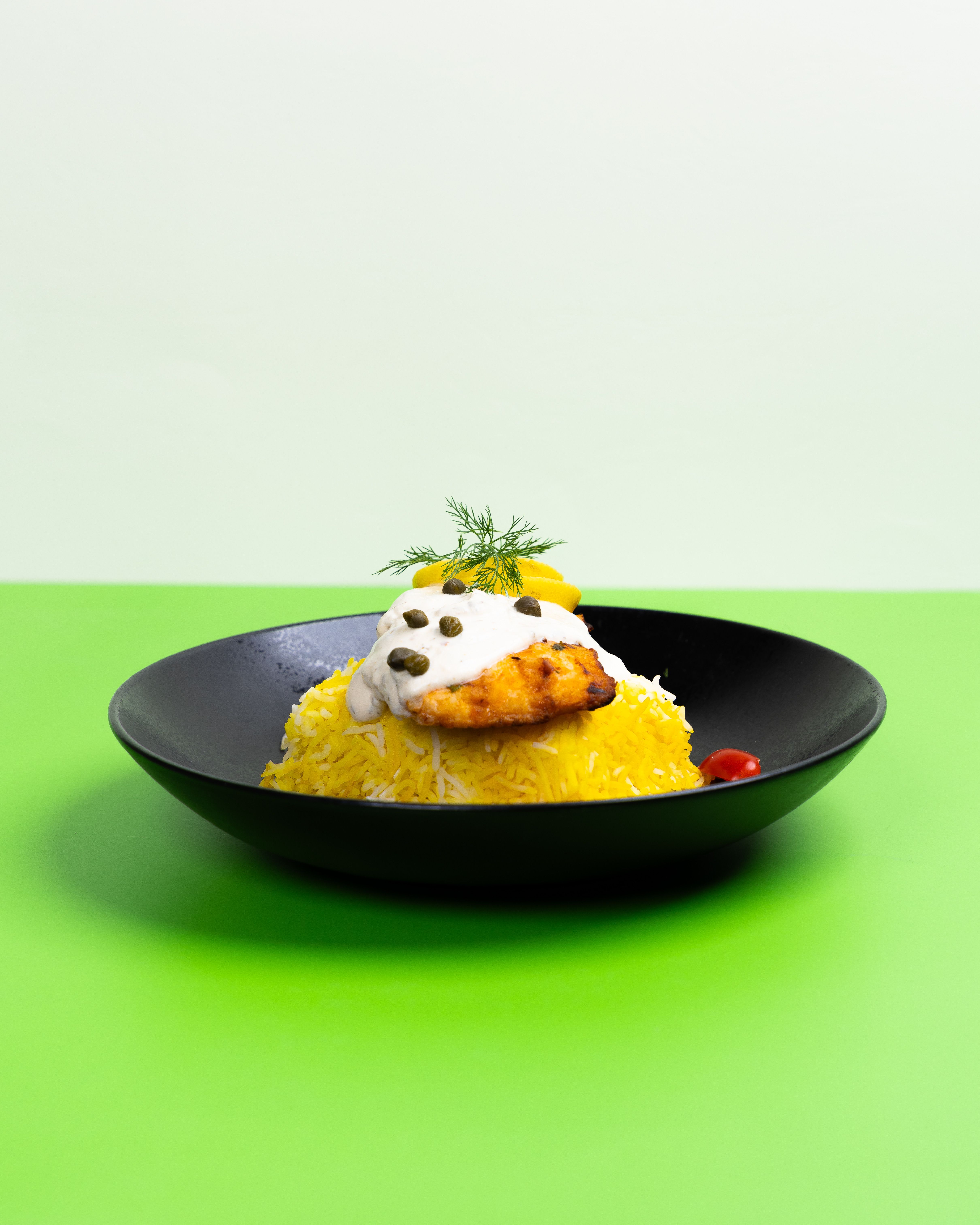 Elegant presentation of yellow rice and creamy chicken sauce in a black bowl over a green backdrop.