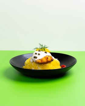 Elegant presentation of yellow rice and creamy chicken sauce in a black bowl over a green backdrop.