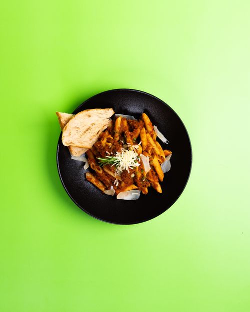 Free Top view of penne pasta with bread in a black bowl on a vibrant green background. Stock Photo