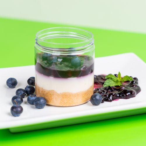 Free Tasty blueberry layered dessert in a jar on a white plate with fresh berries and mint, against a vibrant green background. Stock Photo
