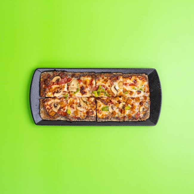 Top view of square pizza slices with cheese and mushrooms on black tray against green background.