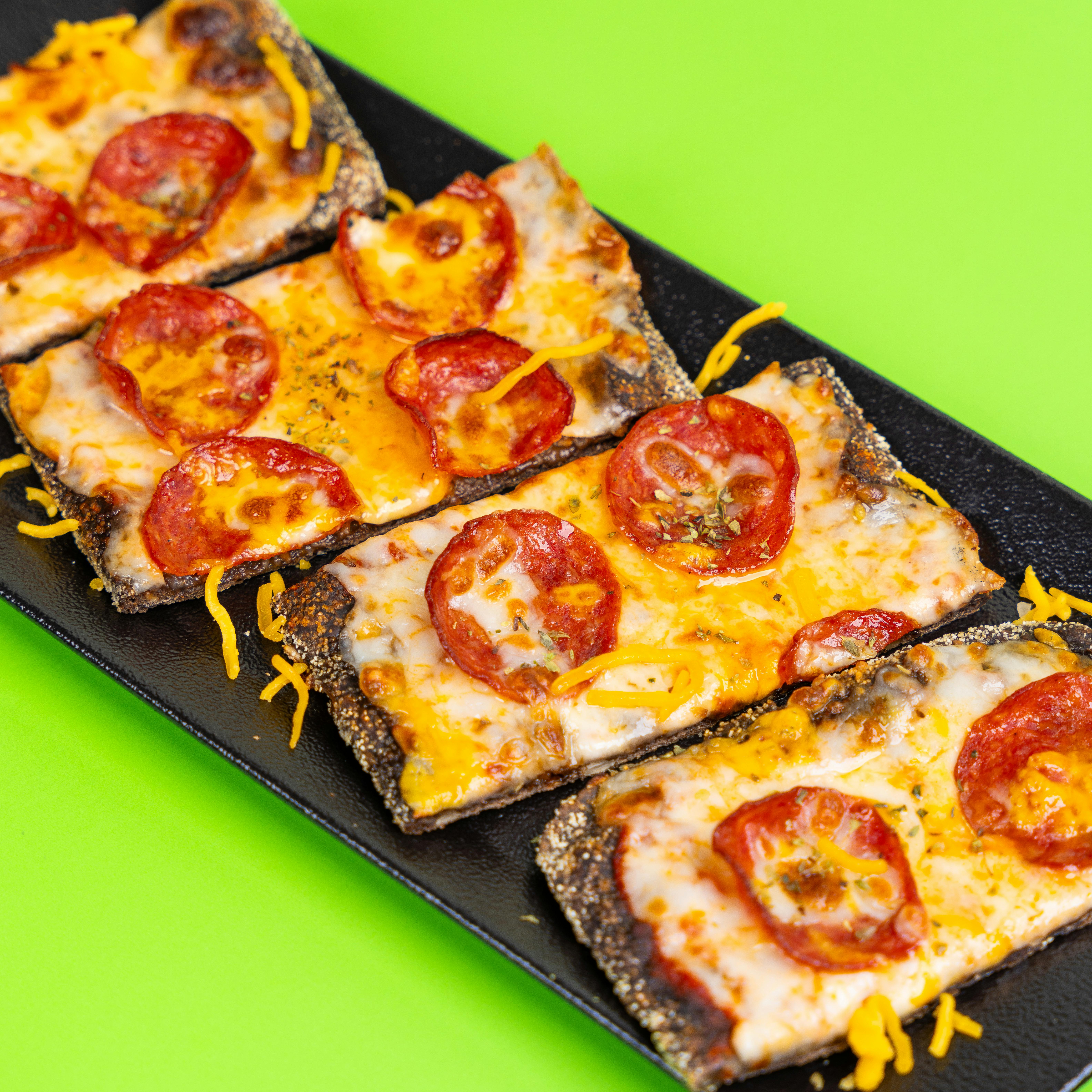 Close-up of cheesy pepperoni pizza slices on a vibrant green background.