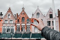 Person Holding Miniature House Toy Comparing on Real Building