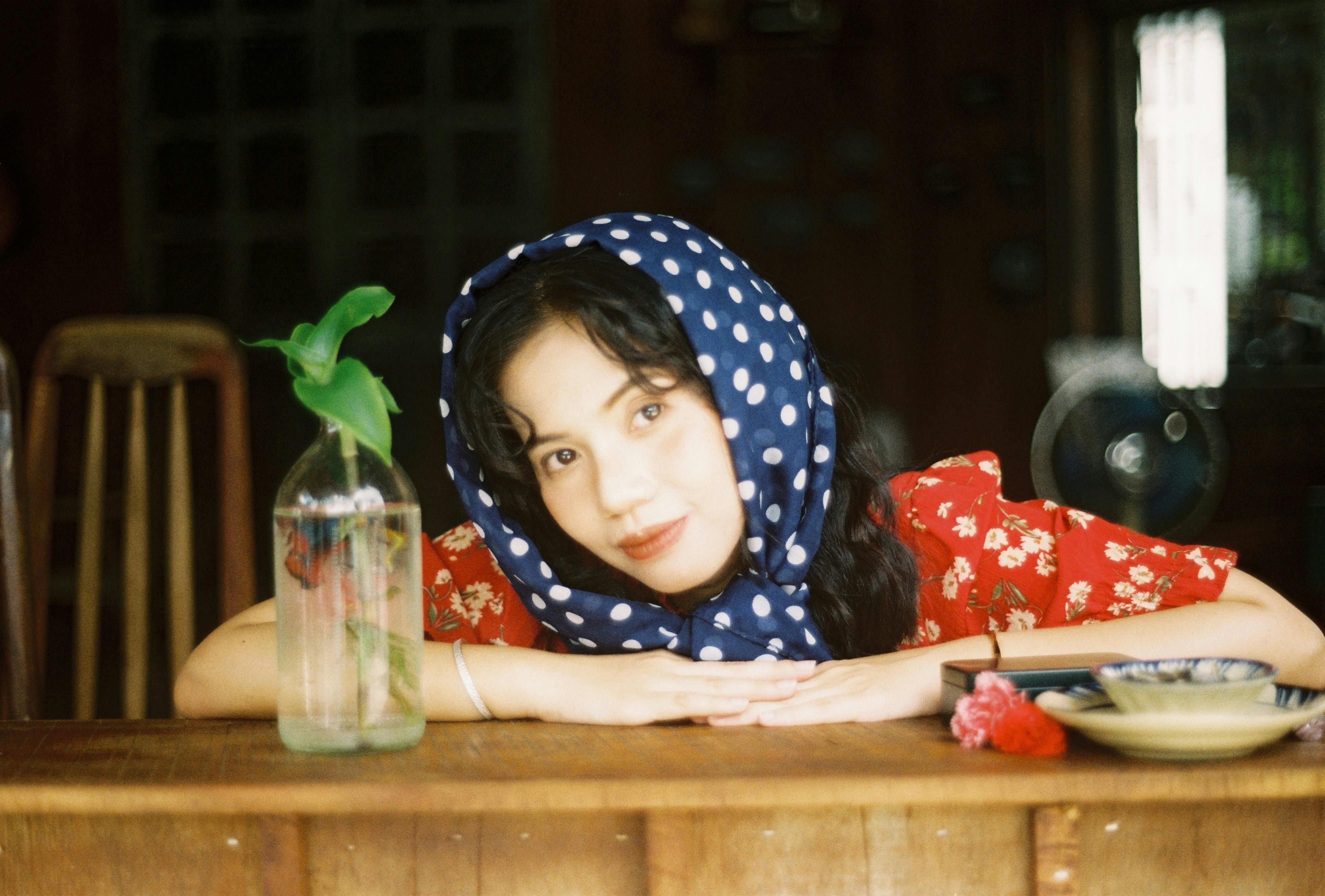 Elegant woman in a polka dot headscarf posing at a bar counter, exuding vintage charm.