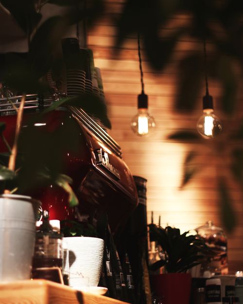 Free Warmly lit cafe interior featuring a professional espresso machine and hanging light bulbs. Stock Photo