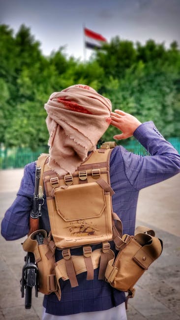 Man with backpack, turban, and tactical gear standing outdoors in Yemen.