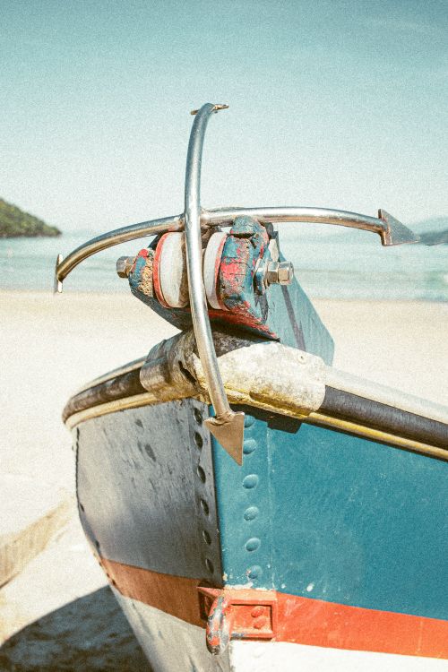 Free A vibrant boat's anchor prominently displayed on a serene sandy beach. Stock Photo