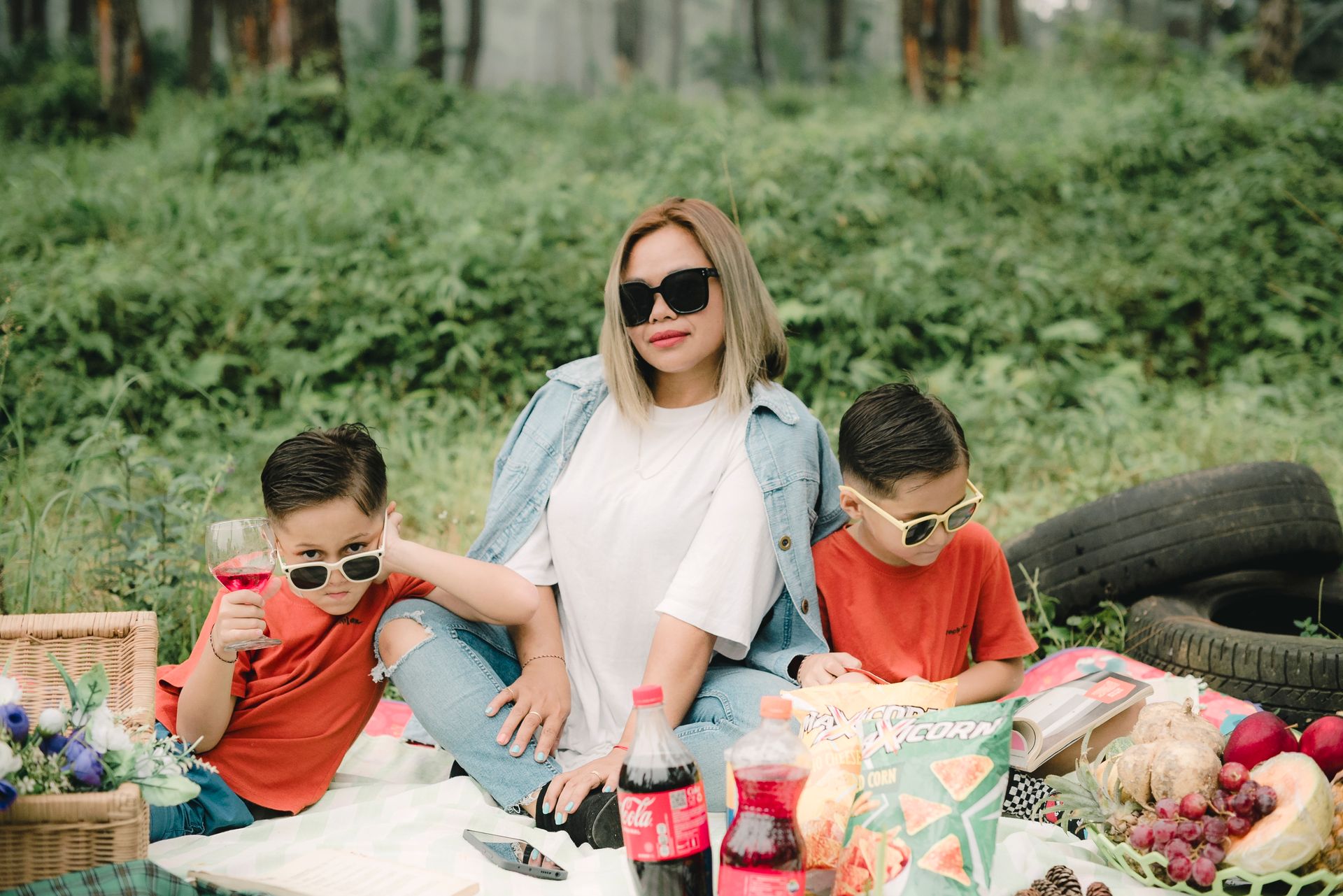 A stylish family enjoying an outdoor picnic with snacks and beverages in a lush setting.