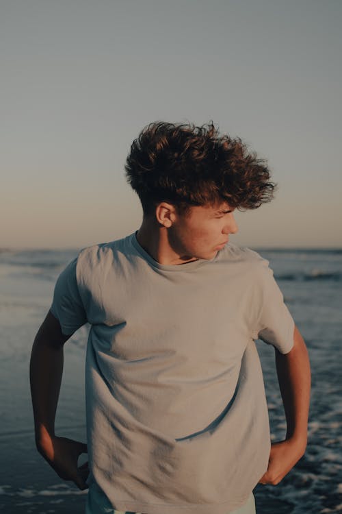 A young man standing on the beach with his hair in his face