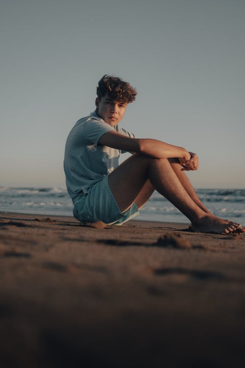 A young man sitting on the beach with his legs crossed