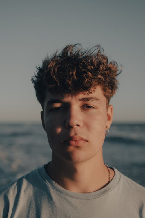 A young man with curly hair standing in front of the ocean