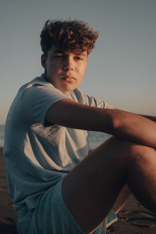 A young man sitting on the beach with his legs crossed