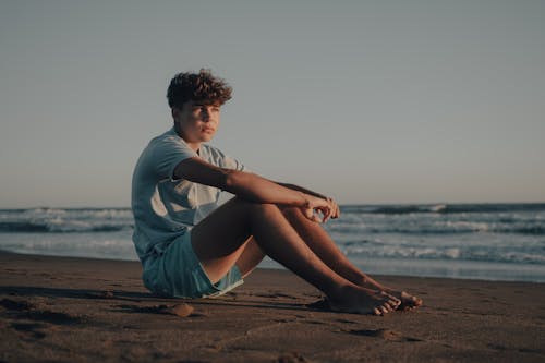 A young man sitting on the beach with his legs crossed