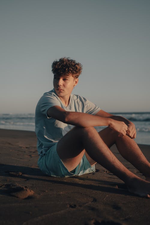 A young man sitting on the beach with his legs crossed