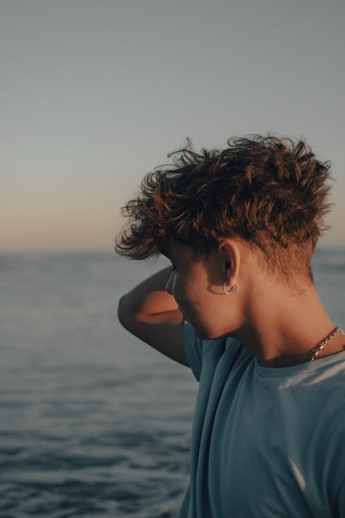 A young man with curly hair standing in front of the ocean