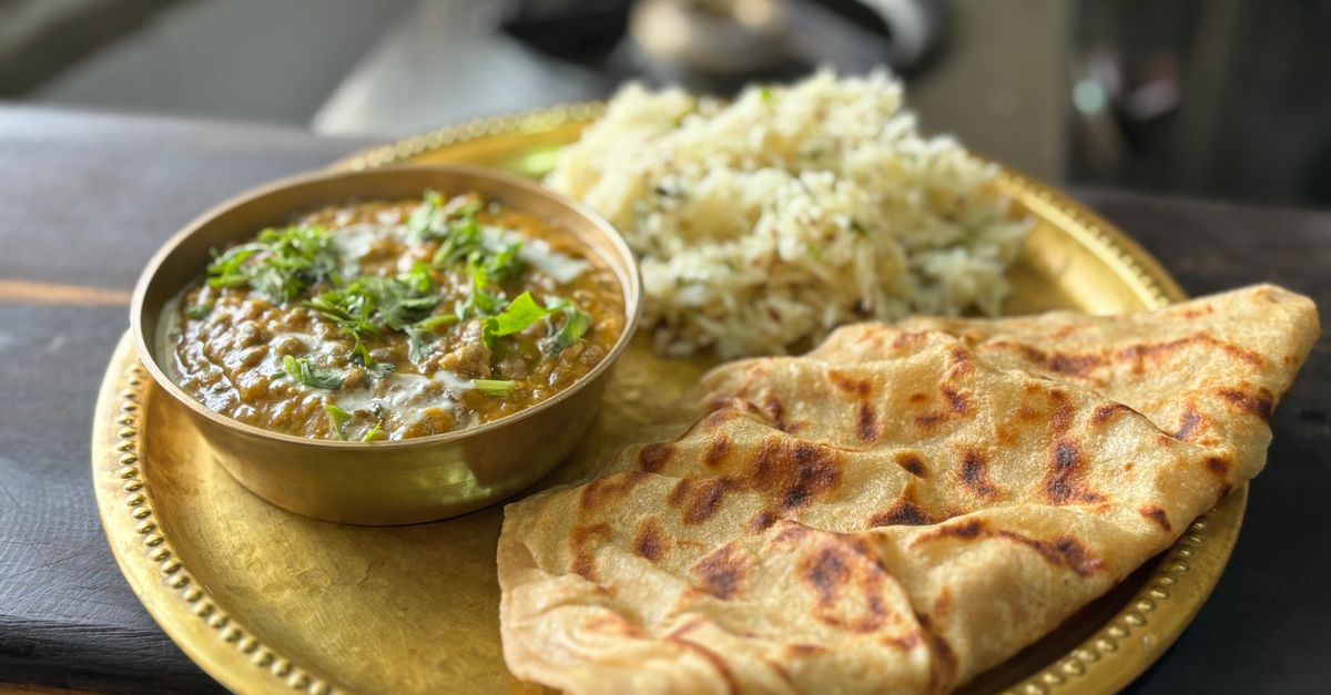 A close-up of a delicious Indian meal with paratha, curry, and rice on a golden plate.