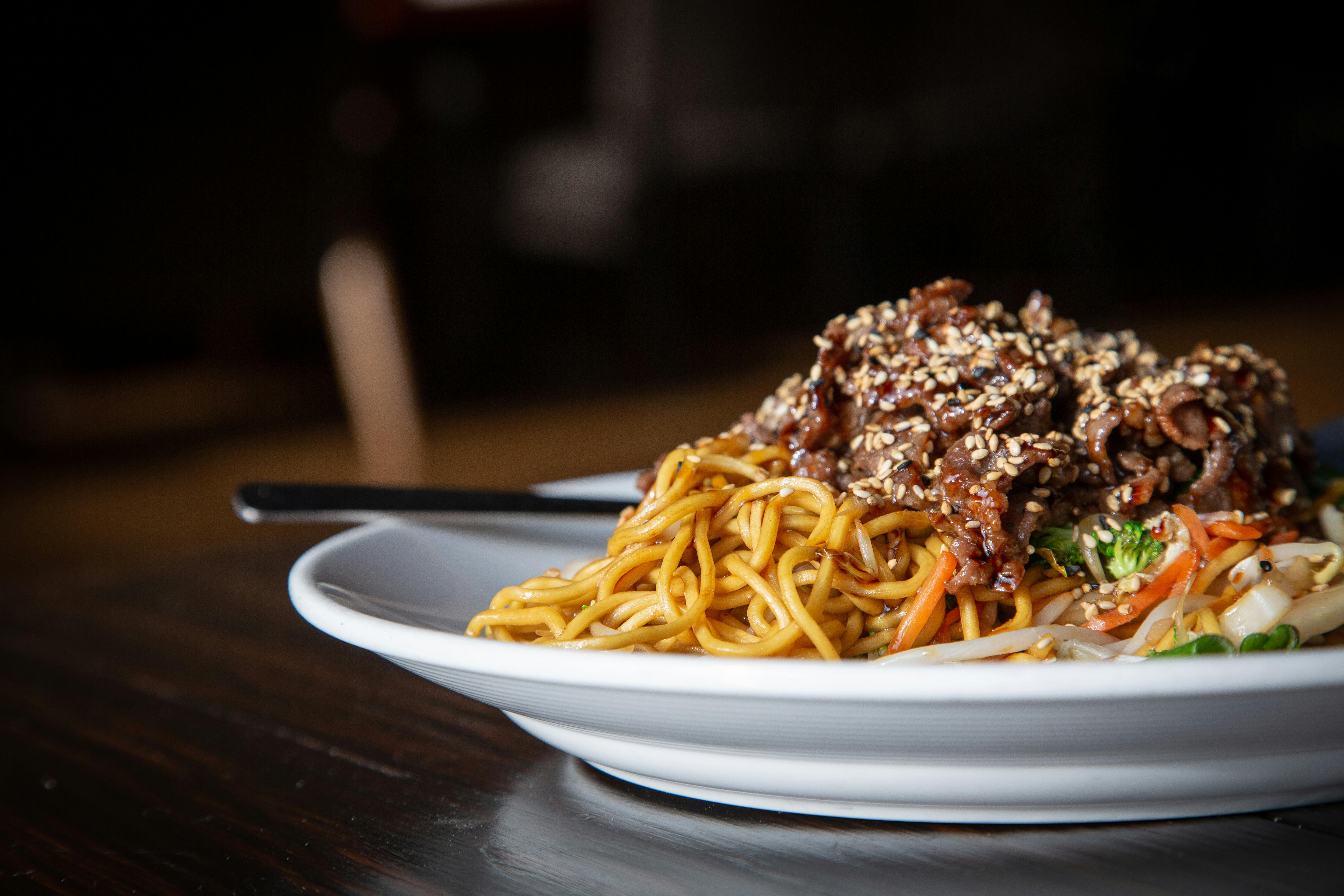 白色盘子上，亚洲牛肉和蔬菜面条的特写镜头，点缀着芝麻