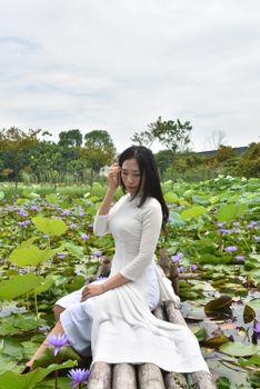 A woman in traditional Ao Dai sits gracefully in a serene lotus pond.
