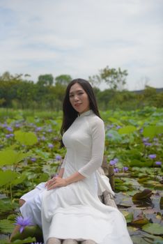 A Vietnamese woman in traditional ao dai sitting gracefully in a lotus pond.